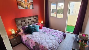 Une chambre dotée d’un grand lit, d’une table de chevet avec une lampe, d’un téléviseur fixé au mur et offrant une vue sur le balcon extérieur.