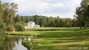 Un parcours de golf doté d’un club-house, d’un étang et entouré d’arbres.