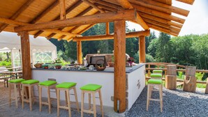 Een houten pergola buiten met een bar, inclusief krukken en een barbecue.