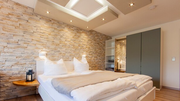 Een moderne slaapkamer met een stenen muur, een bed met witte lakens, een nachtkastje en een ingebouwde boekenkast.