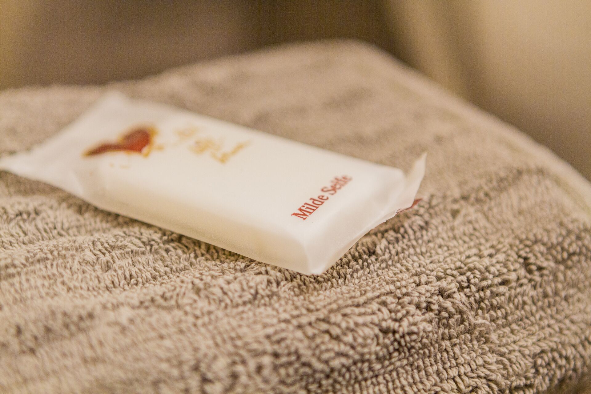 Un pain de savon blanc avec l’inscription « Milde Seife » sur une surface beige texturée.