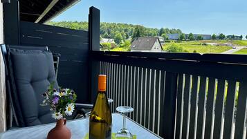 En balkong med ett bord, en flaska vin, ett glas och en vas med blommor.