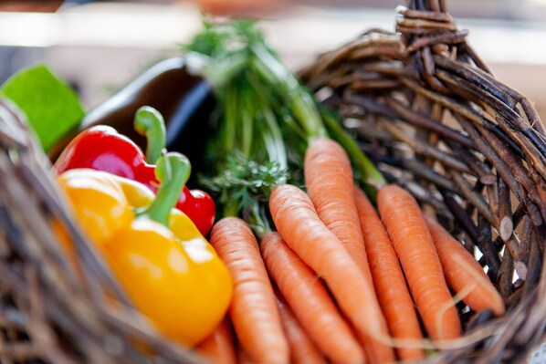 A wicker basket containing carrots, a red bell pepper, and green herbs.