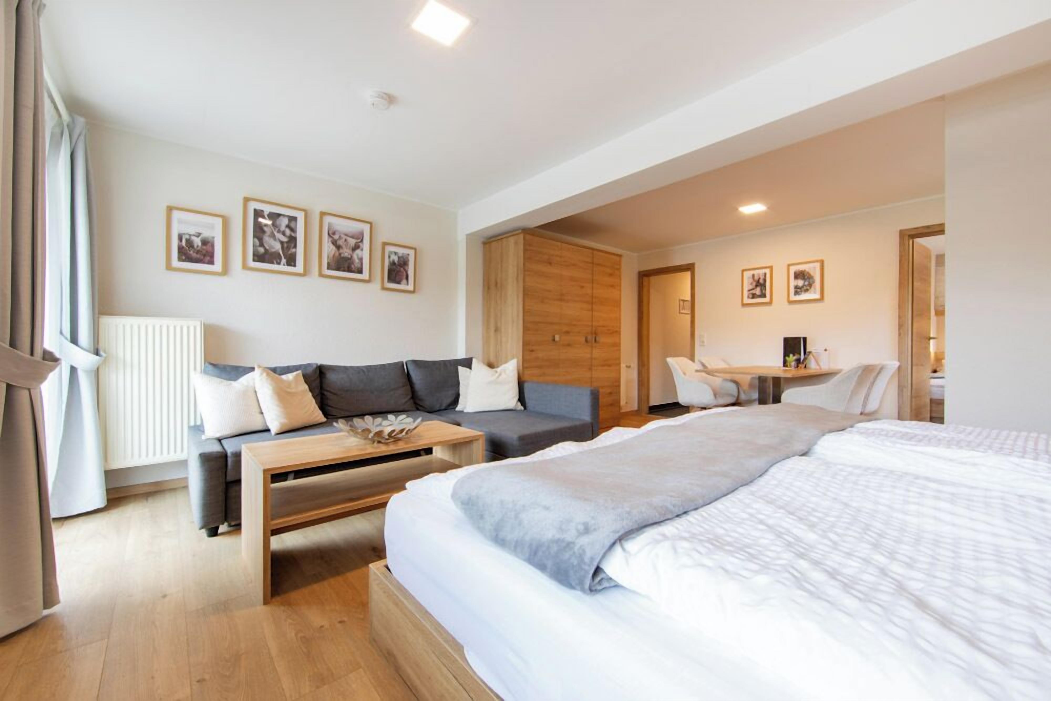 A modern hotel room with a large bed, a sofa, a desk, and a chair.