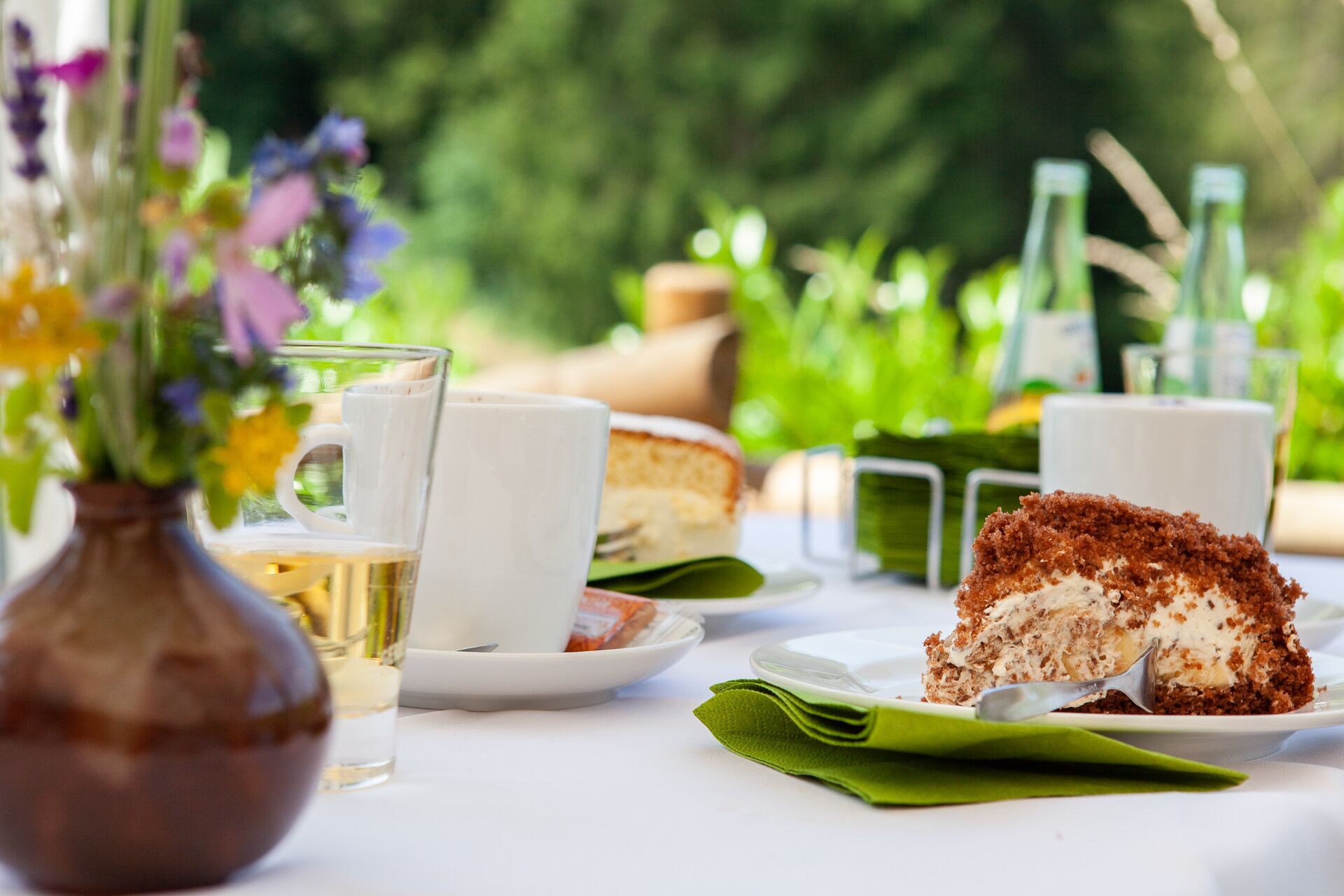 A table set with a slice of cake, a glass of milk, and a vase of flowers.