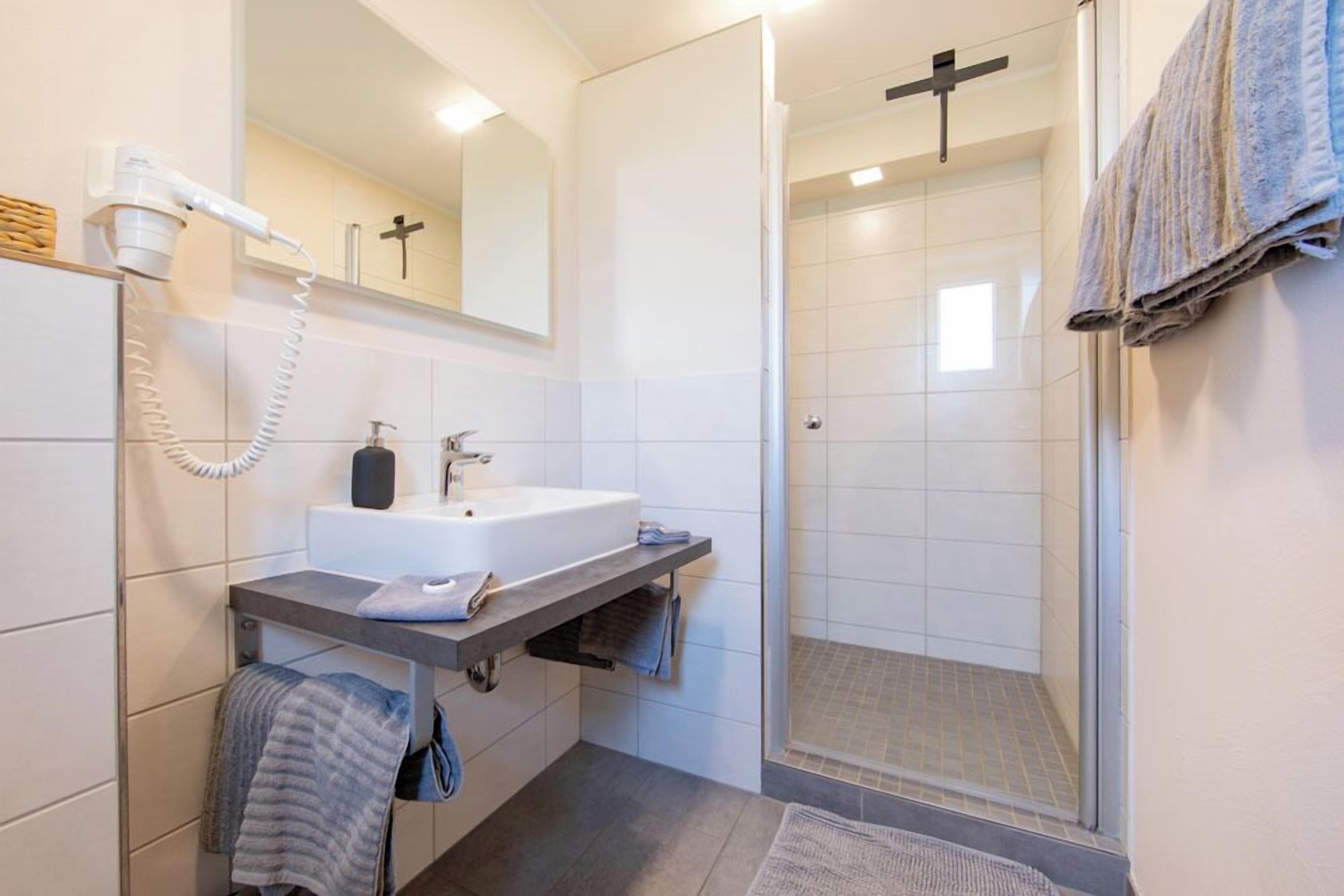 Ein modernes Badezimmer mit einem weißen Waschbecken, einem Spiegel, einem Föhn und einer Duschkabine.