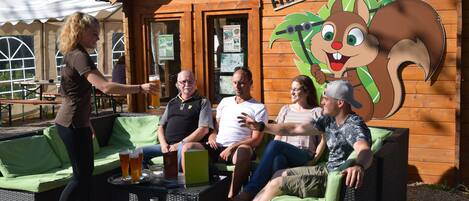 A wooden building with a cartoon squirrel mural, outdoor seating with green cushions, and a table with drinks.