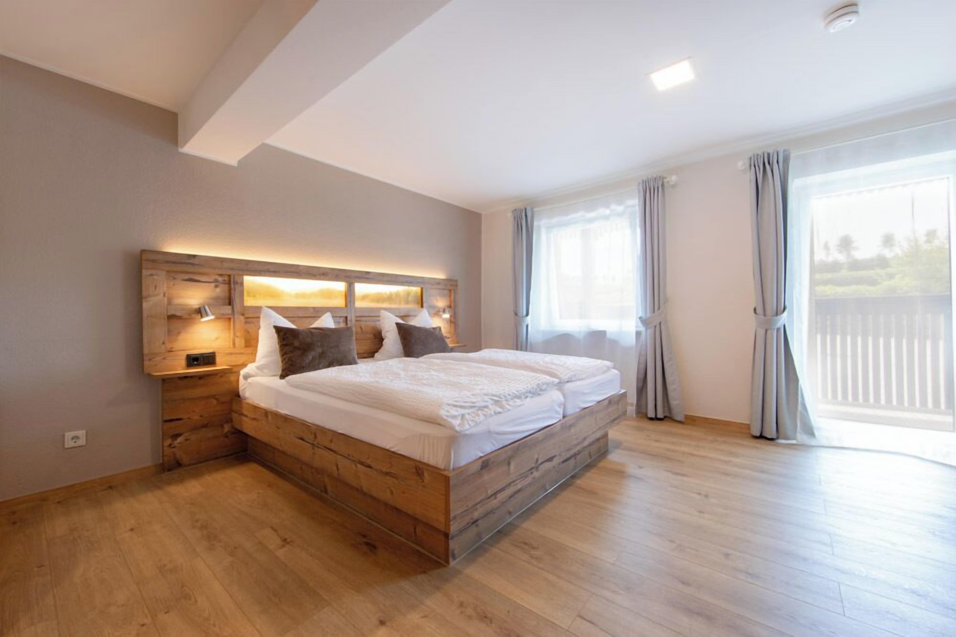 A bedroom with a wooden headboard, a large bed, and a view of the outdoors through a window.