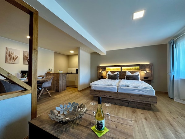 Une chambre d’hôtel moderne avec un lit en bois, un coin repas et une cuisine en arrière-plan.