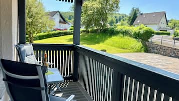 A covered outdoor seating area with a table and chairs, overlooking a well-maintained garden and houses.