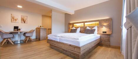 A bedroom with a wooden bed, a desk, two chairs, and a wall-mounted lamp.