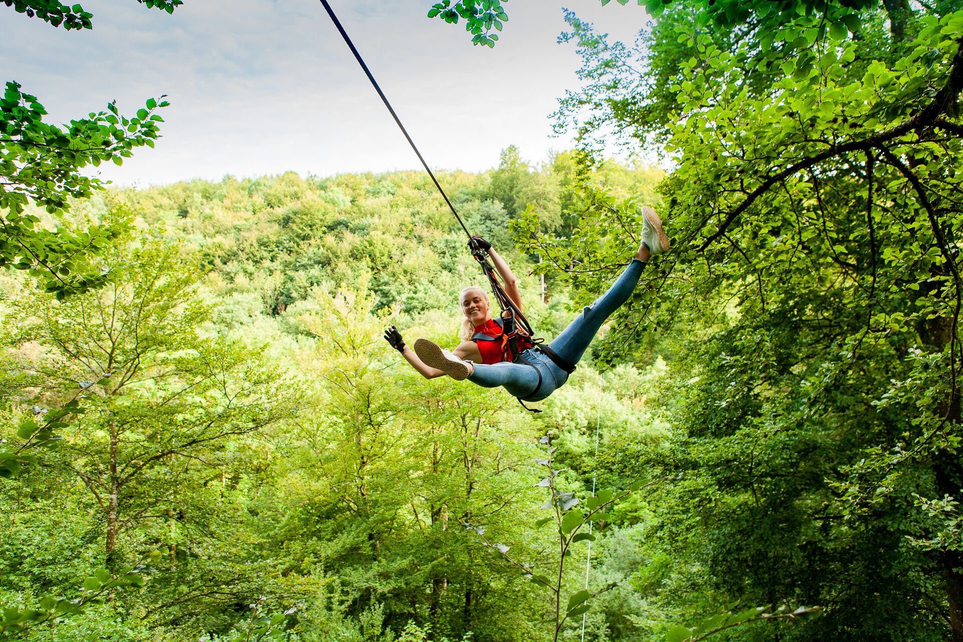 A person suspended in mid-air by a zip line in a forested area.