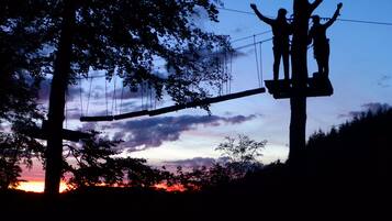 A silhouette of two people on a zip line against a sunset sky.