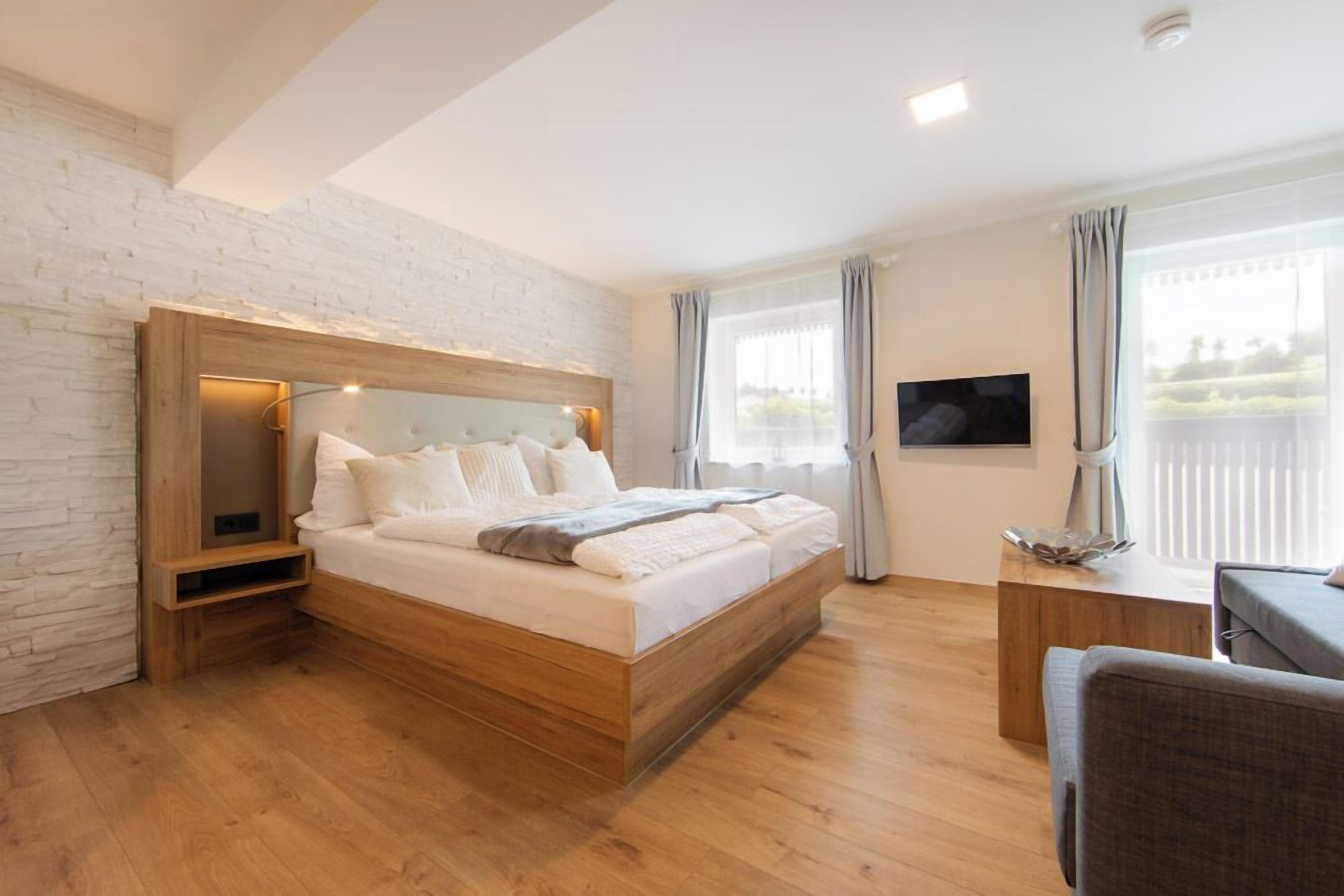 A modern bedroom with a wooden bed, a flat-screen TV, and a desk with a chair.