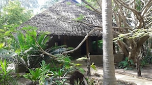 Eine strohgedeckte Hütte, umgeben von üppiger Vegetation und einem großen Baum.