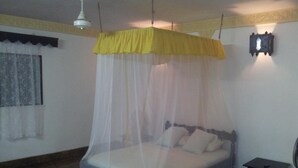Ein Zimmer mit einem Bett unter einem gelben Baldachin, einem kleinen Tisch und einer Wandleuchte.