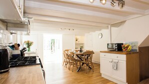 A modern kitchen with wooden flooring, a dining area with wooden chairs, and a white cabinet with a microwave. - 4 bedroom accommodation in Kirkcudbright (Kirkcudbright)
