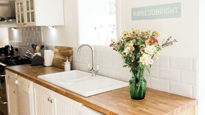 A kitchen with a wooden countertop, a white sink, and a green vase with flowers. There is a sign on the wall that reads "KIRKCUDBRIGHT". - 4 bedroom accommodation in Kirkcudbright (Kirkcudbright)