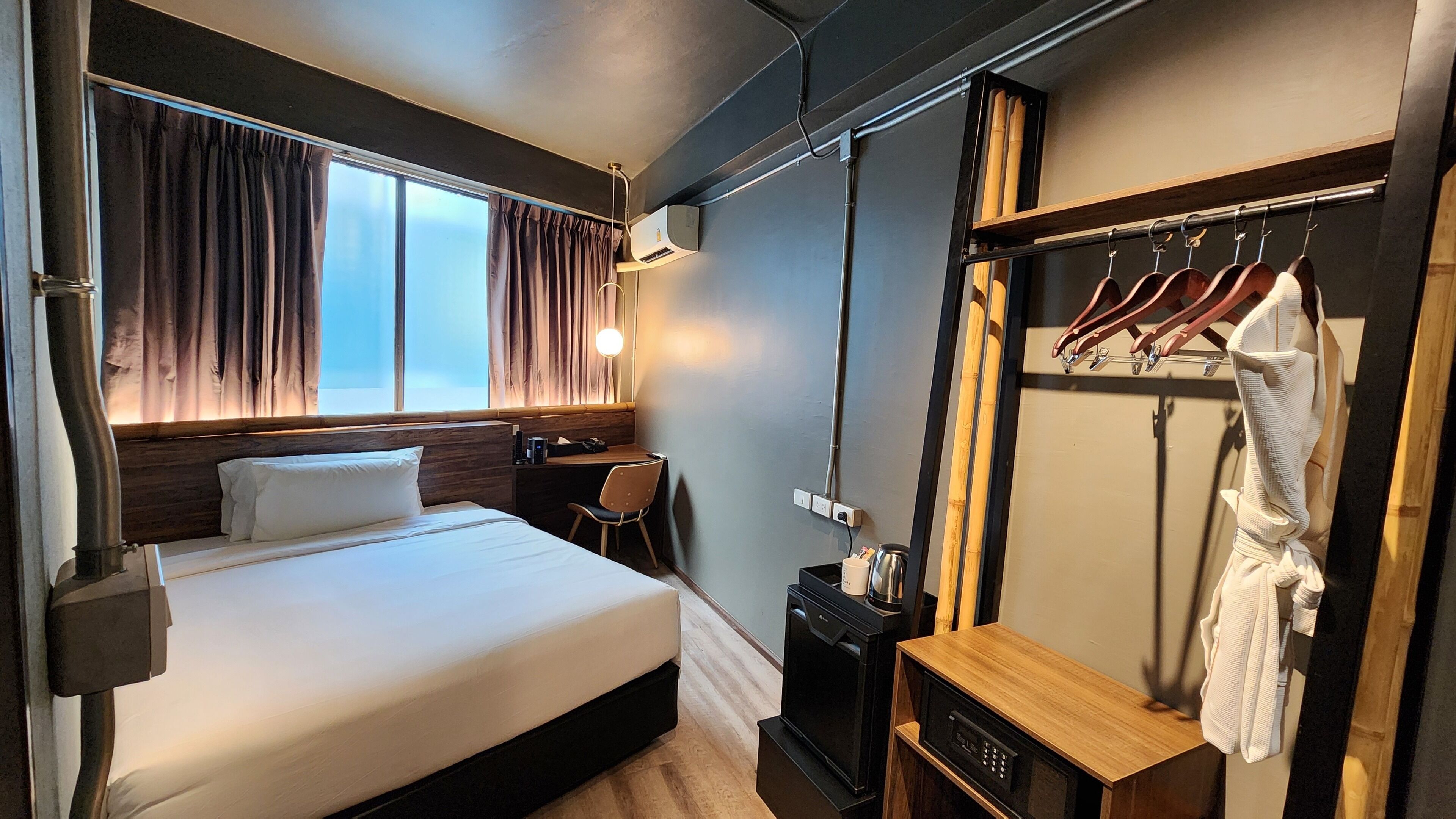 Hotellihuone, jossa on sänky, työpöytä, tuoli, vaatekaappi ja peili.