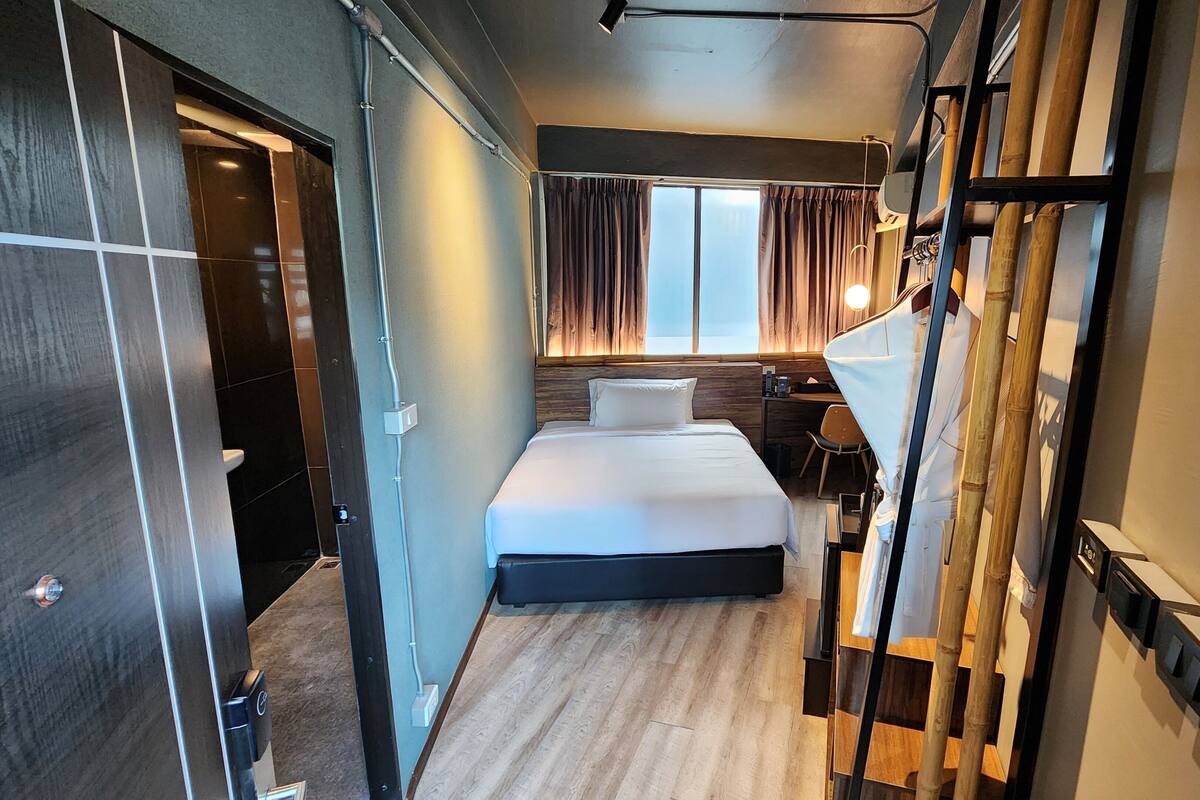 A hotel room with a bed, a desk, and a window with curtains.