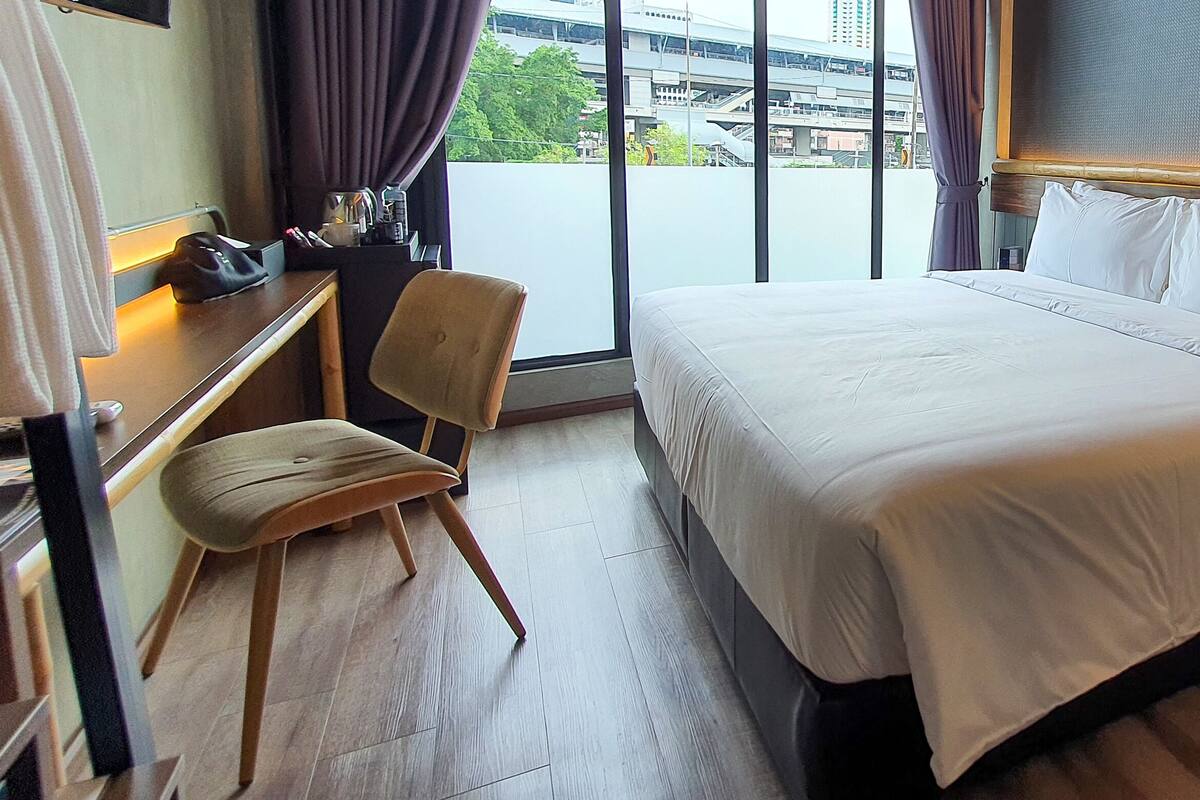 A hotel room with a large bed, a desk, a chair, and a small table.