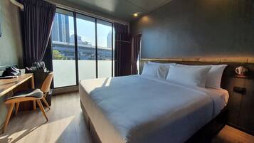 Une chambre d’hôtel avec un grand lit, un bureau et une chaise. Les fenêtres offrent une vue sur la ville.