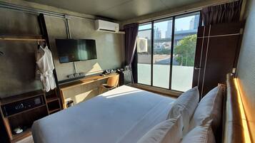 A hotel room with a large bed, a desk with a chair, a TV mounted on the wall, and a window with a city view.