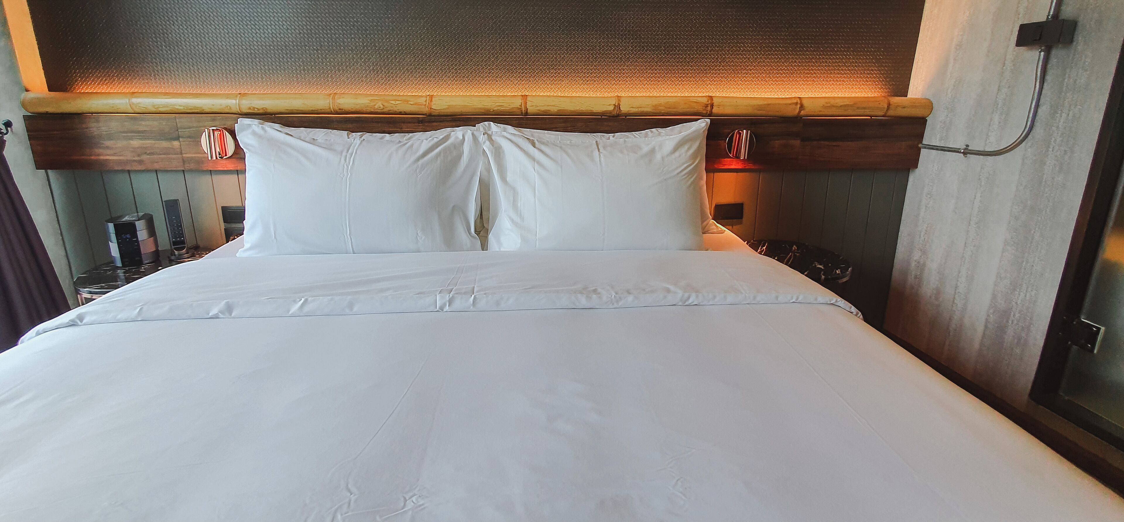 A neatly made bed with white linens, a wooden headboard, and a wall-mounted light fixture.