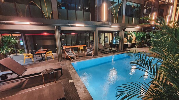 An indoor swimming pool with lounge chairs and tables, surrounded by glass walls and indoor plants. - Hotel Ordinary Bangkok (Bangkok)