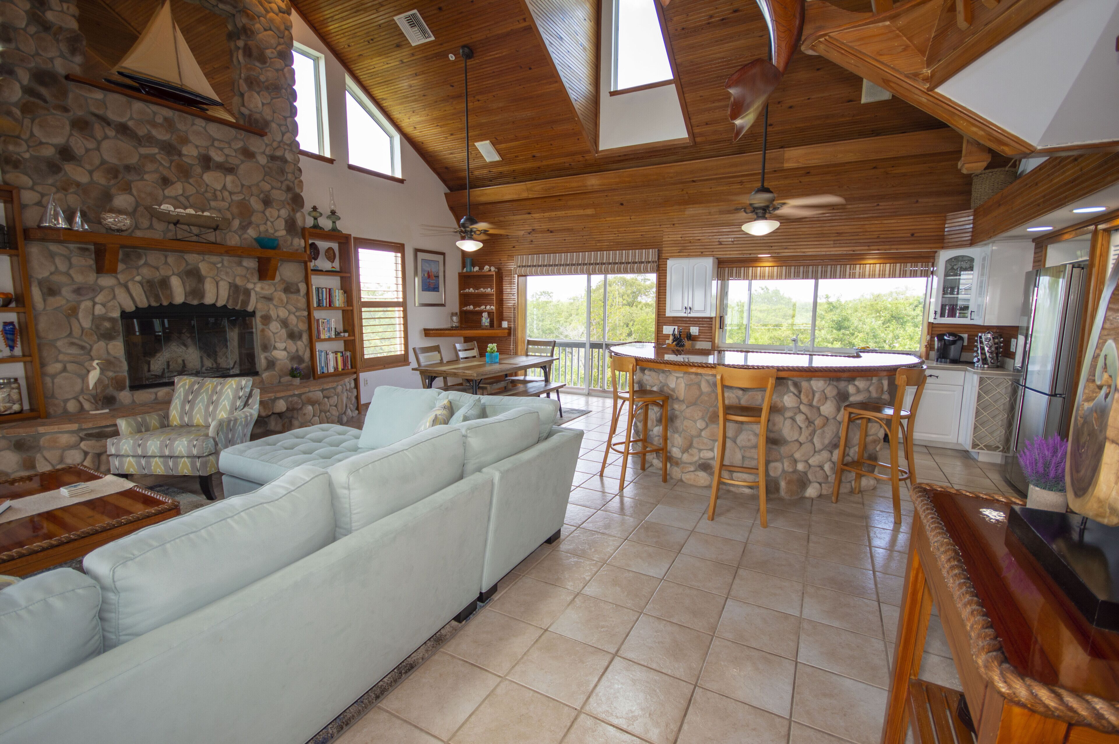 A spacious living room with a stone fireplace, a large light-colored sofa, and a wooden dining area with a stone accent wall.