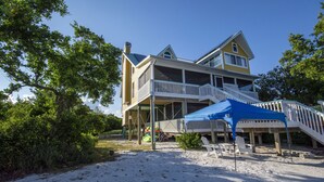 A two-story beach house with a balcony, a covered patio, and a sandy beach area. - Remember When, Old Florida Beach House (Cayo Costa)