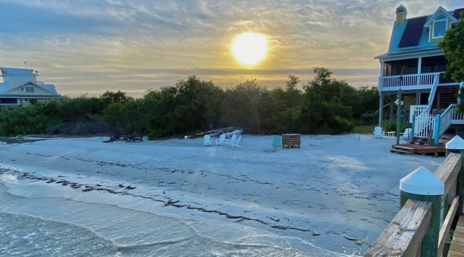 Ein Strand mit Sonnenuntergang, einer Holzlattenveranda und einem Gebäude mit Balkon.