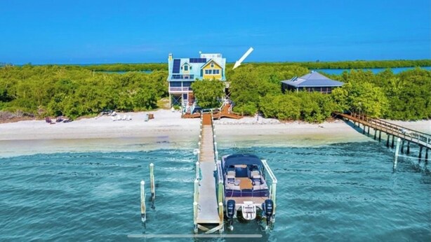 A house with a dock extending into the water, surrounded by lush greenery and a clear blue sky. - Remember When, Old Florida Beach House (Cayo Costa)
