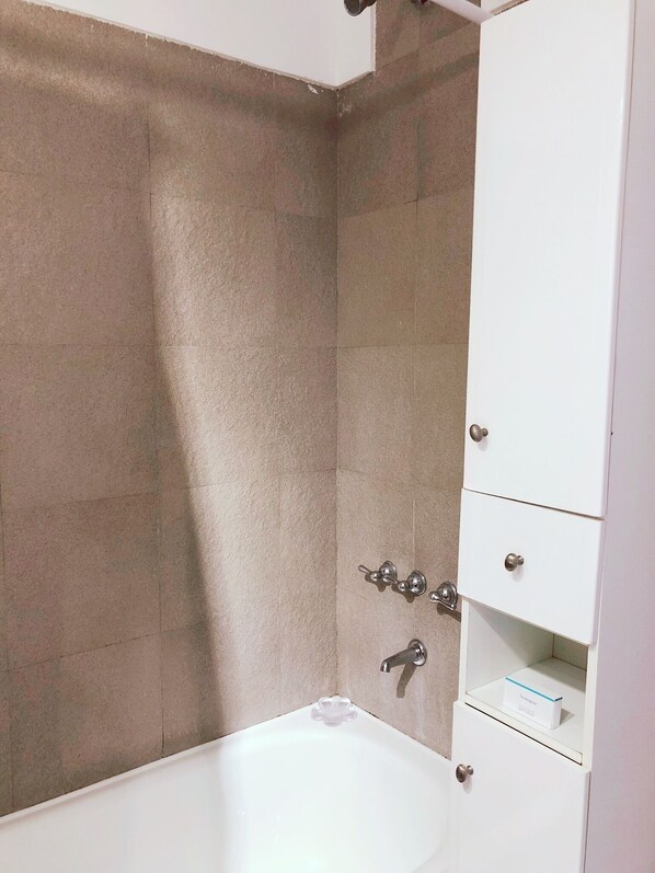 A bathroom with a bathtub, a shower, and a white cabinet with drawers.