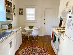 Cocina compacta con alacenas blancas, estufa a gas, microondas, tostadora y una mesa de comedor con sillas.