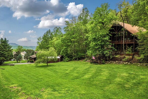 A cabin surrounded by lush greenery, with a clear sky and distant mountains.