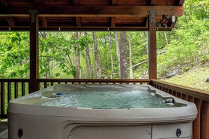 A hot tub under a wooden deck with a forest view.