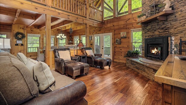 A spacious log cabin interior with a large wooden ceiling, a stone fireplace, and a cozy seating area with leather sofas and ottomans. - Free Tickets | Creek-Side, Views, INSANE Arcade, Yard, Fireplace (Sevierville)