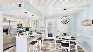Una cocina con armarios blancos, un refrigerador de acero inoxidable, un horno empotrado y un comedor con una mesa redonda y sillas blancas.