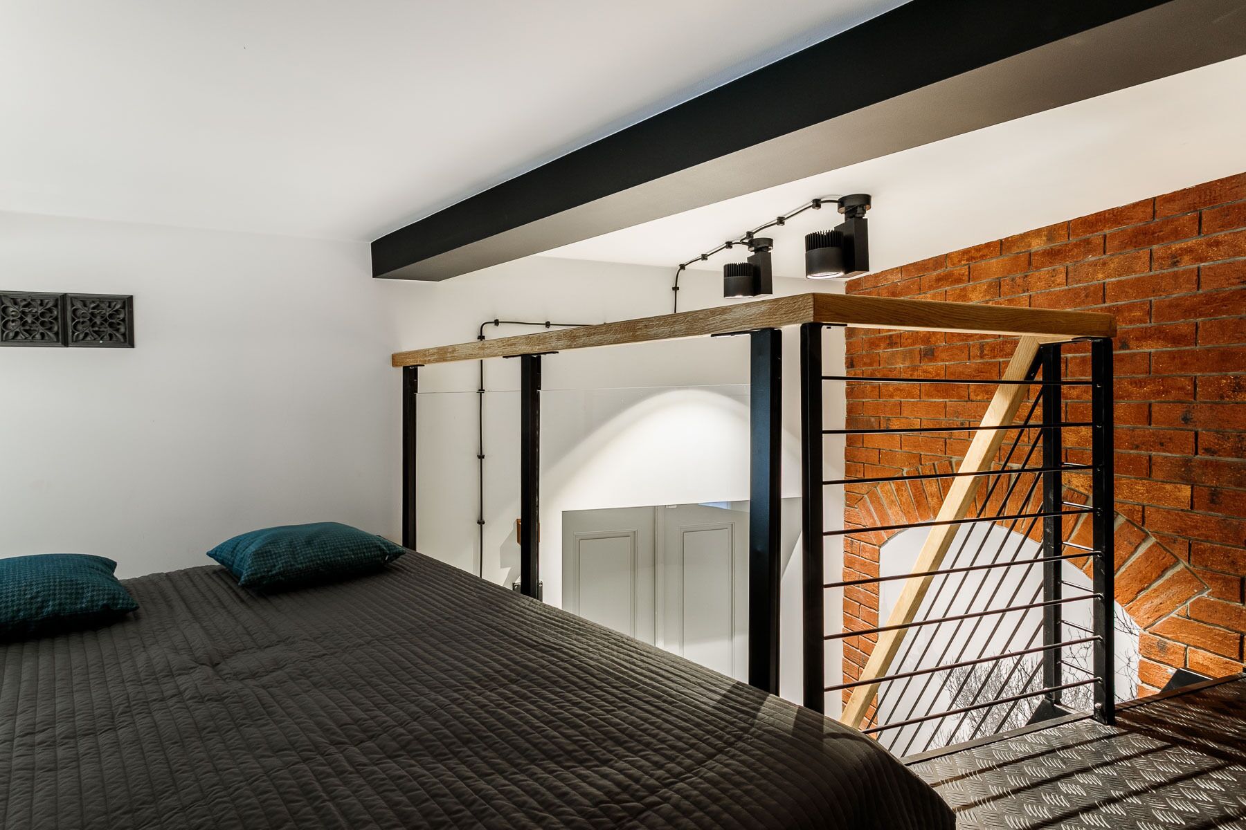 Een slaapkamer met een bed, een houten balk, een bakstenen muur en een trap.