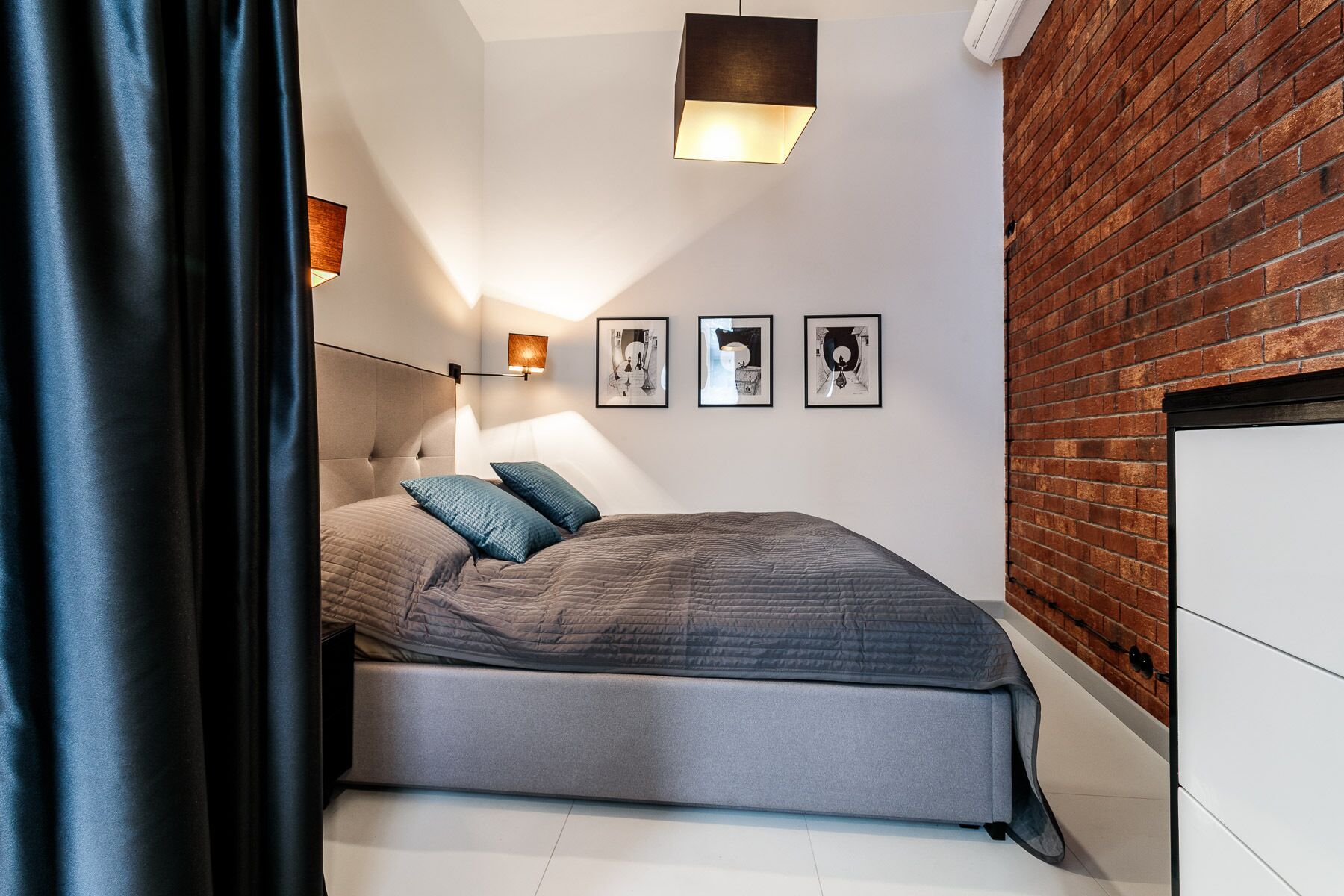 A modern bedroom with a bed, a wall-mounted light, and three framed pictures.