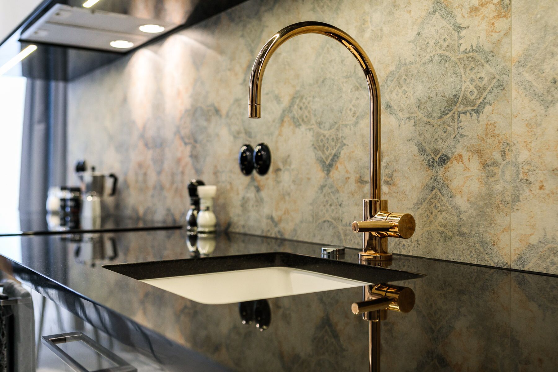 A modern kitchen with a sleek black countertop, a gold faucet, and a marble backsplash.