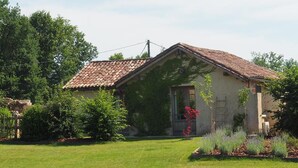 Una casa de un piso con techo de tejas, rodeada de un césped cuidado y diversas plantas.