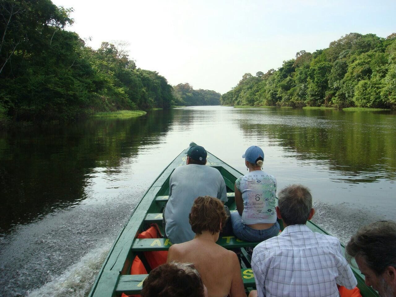 Un grupo de personas en un bote verde en un río tranquilo rodeado de abundante vegetación.
