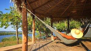 A hammock under a thatched roof, wooden deck, and a view of a lake. - Anaconda Amazon Resort (Manaus)