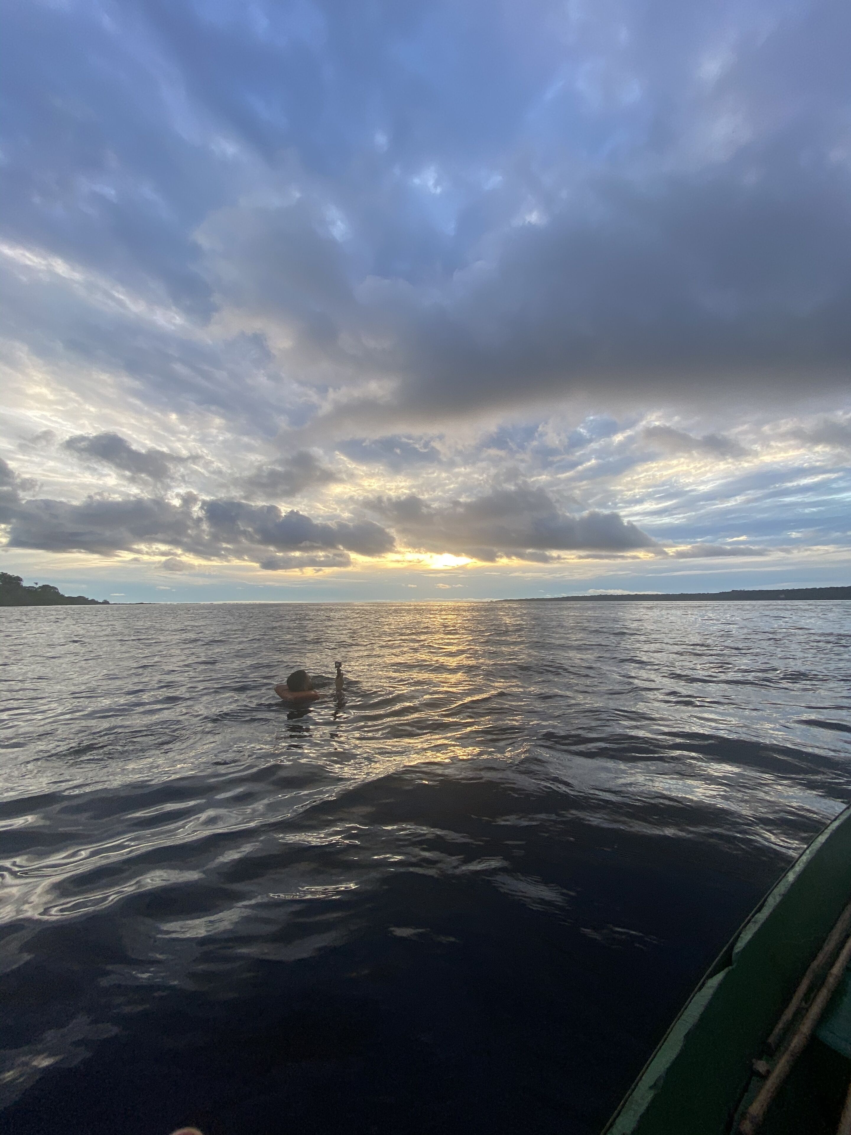 A body of water with a boat in the foreground and a sunset in the background.