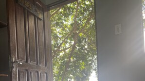 A room with a bed, a pair of sunglasses, and a hat on the bed. There is a wooden door and a window with a view of trees and water. - Anaconda Amazon Resort (Manaus)