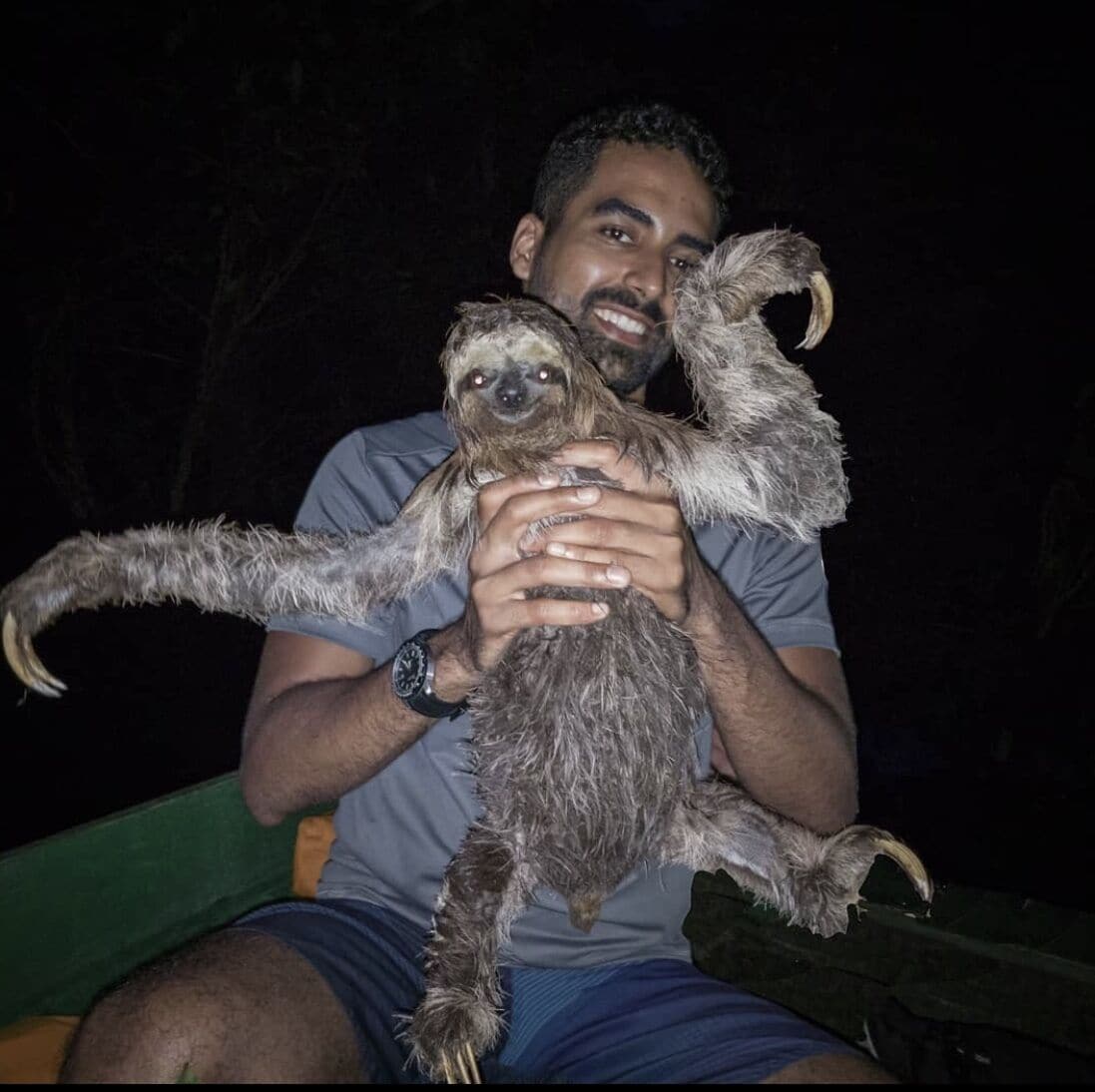 A person holding a sloth with long limbs and a curved tail.