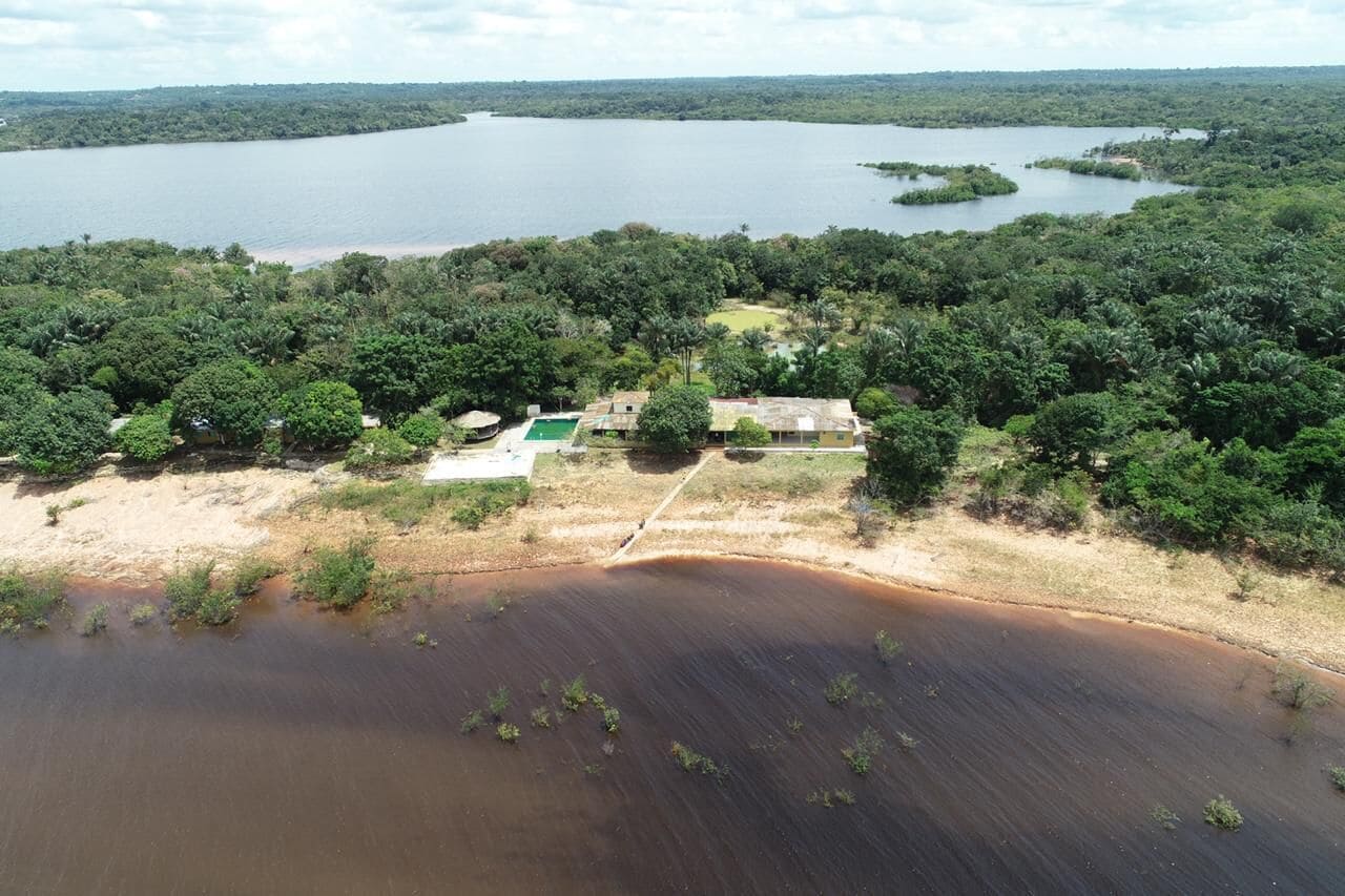An aerial view of a property with a large body of water, dense greenery, and a few buildings.