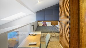 Een moderne slaapkamer met schuine wand, een bed met hoofdeinde, een bureau met lamp en uitzicht op de omgeving.